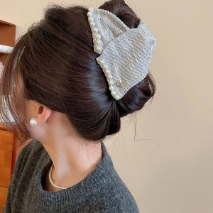 Detail of grey fabric hair claw with pearl trim on model's hair in an elegant hairstyle