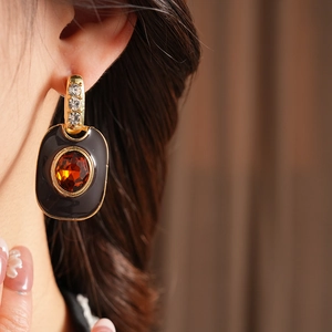 Detail view of a vintage enamel earring with amber gemstone and gold-tone metal finish
