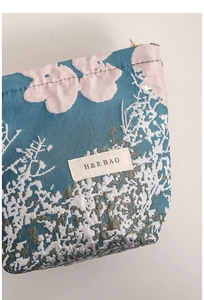 Detail of blue jacquard cosmetic bag with pink floral patterns and gold zipper