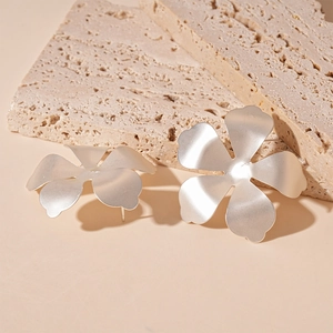 Close-up of matte silver flower stud earrings on natural beige travertine stone