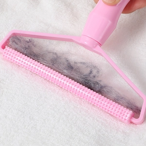 Pink manual lint remover tool for sweaters and coats shown cleaning gray fabric fuzz