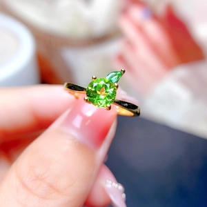 Close-up of a gold ring featuring a round green gemstone and marquise accents on a model
