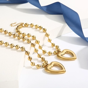 Detailed view of gold beaded chain necklace with hollow heart pendants on a white pedestal