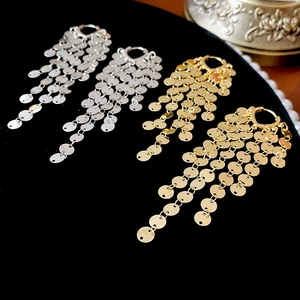 Close-up of gold and silver layered disc fringe tassel earrings on a velvet background