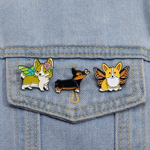 Détail de trois épingles en émail Corgi avec ailes et papillons sur tissu en denim bleu