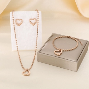 Parure de bijoux en or rose avec pendentifs cœur et chaîne à billes sur marbre