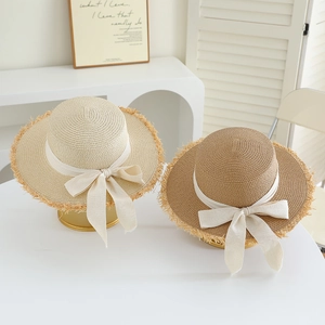 Detail of two straw hats with ribbon bows and raw fringe edges on a white table
