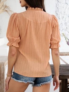 Detail view of orange blouse featuring flare sleeves and textured pleated fabric design