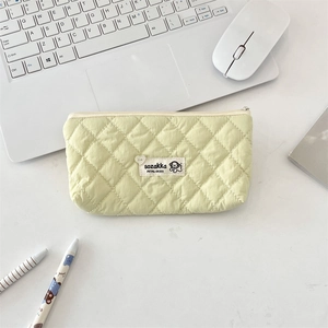 Quilted cosmetic bag with diamond patterns on a desk near a laptop and stationery