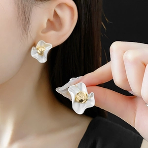 Detail of white flower stud earrings with gold stamen worn by model and held by hand