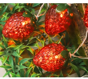 Dettaglio della ghirlanda luminosa a LED fragola rossa con foglie verdi e luce calda