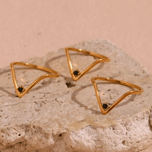 Close-up of three thin gold V-shaped rings with micro-set black stones on a stone base