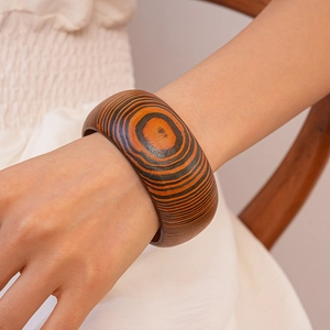 Detail of a wide wooden bangle with orange and black concentric geometric patterns on wrist