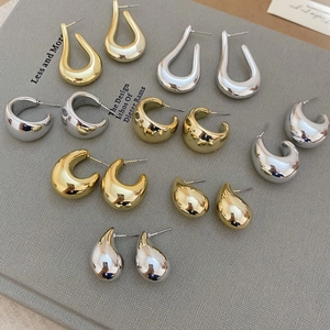 Detailed close-up of various geometric C-shaped gold and silver earrings on a textured board