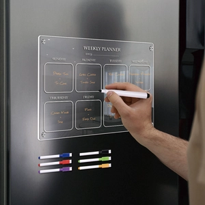 Close-up of hand writing on clear magnetic acrylic weekly planner on a refrigerator