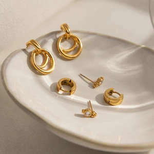 Detailed view of three pairs of gold geometric earrings with zircons on a ceramic tray