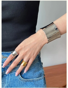 Close-up of a silver wide curved cuff bracelet and matching rings worn by a model