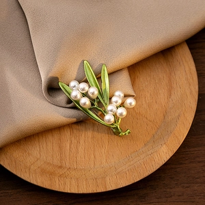 Detail of green enamel olive leaf brooch with white pearls on a wooden display