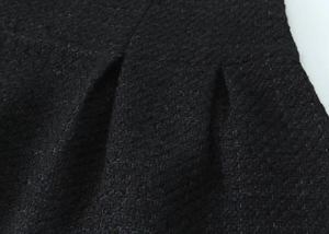 Detailed macro view of black tweed fabric with intricate pleat design and woven texture