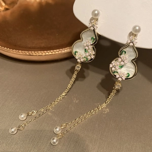 Detail view of gold earrings with pearl tassels, pink flower motifs and gourd shape