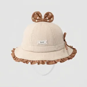 Detail eines Baby-Cordhutes mit beigem Stoff, braunen Rüschen und einer gepunkteten Schleife