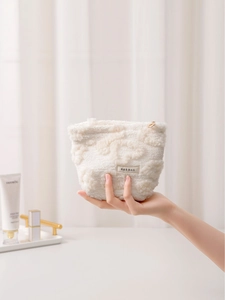 Creamy white plush heart makeup bag with embossed pattern held by a hand in soft light