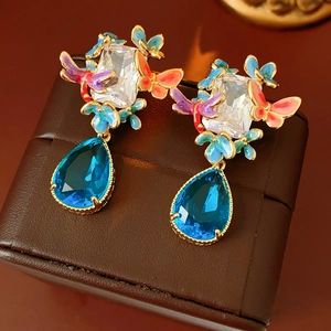Detailed macro of vintage enamel butterfly earrings with blue teardrop gemstone pendants
