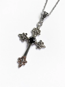 Macro detail of gothic silver cross pendant with a black round gemstone and textures