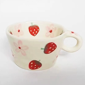 Close-up of hand-painted red strawberries and pink flowers on a beige ceramic mug