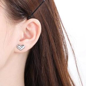 Close-up of elegant silver heart stud earrings worn on a model with a clean white background