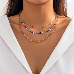 Close-up of layered gold chain necklace featuring colorful resin beads on white shirt