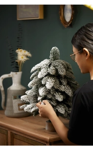 Close-up of a hand touching a mini flocked PE Christmas tree with realistic snow effect