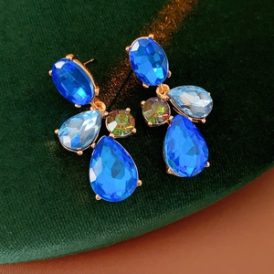 Detailed close-up of blue geometric teardrop earrings on green velvet background