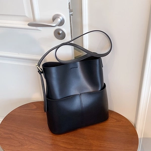 Minimalistische schwarze Leder-Eimertasche mit Schultergurt auf einem Holztisch