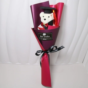 Detail view of graduation plush bear in black cap and gown within purple gift wrap