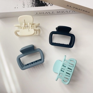 Flat lay of small square hollow hair claws in cream, black, and blue tones on white table
