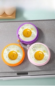 Three colorful silicone egg rings in purple, orange, and pink on a non-stick pan