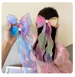 Detail of colorful organza bow hair clip with pearls, rhinestones and long wavy ribbons