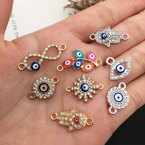 Evil eye and hamsa jewelry connectors in hand showing scale and colorful enamel detail
