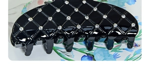 Close-up of a large black glossy hair claw clip featuring a sparkling diamond lattice pattern