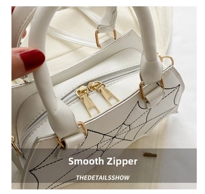 Close-up of golden dual zippers and spiderweb print details on a white PU handbag