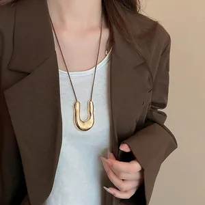 Collana con ciondolo a U dorato e cordino marrone, indossata su un elegante blazer marrone