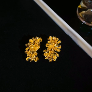 Macro shot of gold floral C-shaped metal earrings with layered petal detail and high gloss