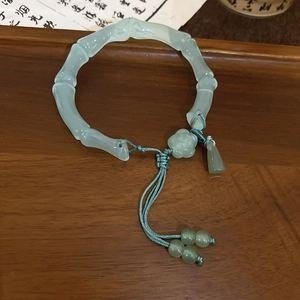 Bracelet style bambou vert clair avec pendentif fleuri sur plateau en bois sombre