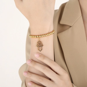 Close-up of a golden beaded bracelet featuring a Hamsa hand charm on a female wrist