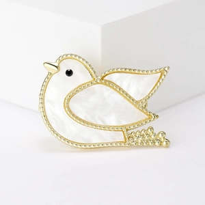 Elegant gold-tone pigeon brooch with white shell inlay on a minimalist white background