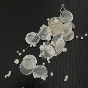 Macro detail of cascading shell discs and white pearls on long tassel clip-on earring