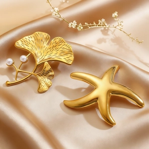 Detail of golden ginkgo leaf and starfish brooches with pearls on champagne silk fabric