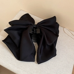 Close-up of a large black fabric bow hair claw clip on a textured decorative base