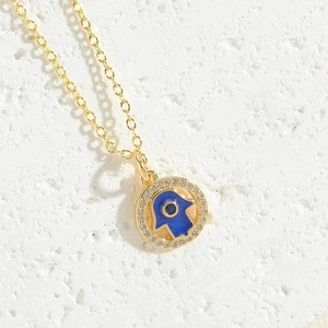 Detail of a golden Hamsa Hand pendant with a blue Evil Eye and white zircon stones